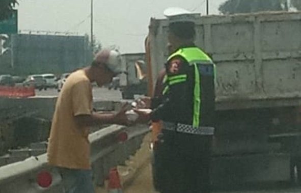Bripka Taufan dari PJR BSD Korlantas Polri membagikan nasi kotak kepada sopir yang kendaraannya rusak di Tol BSD sambil menyampaikan pesan keselamatan.